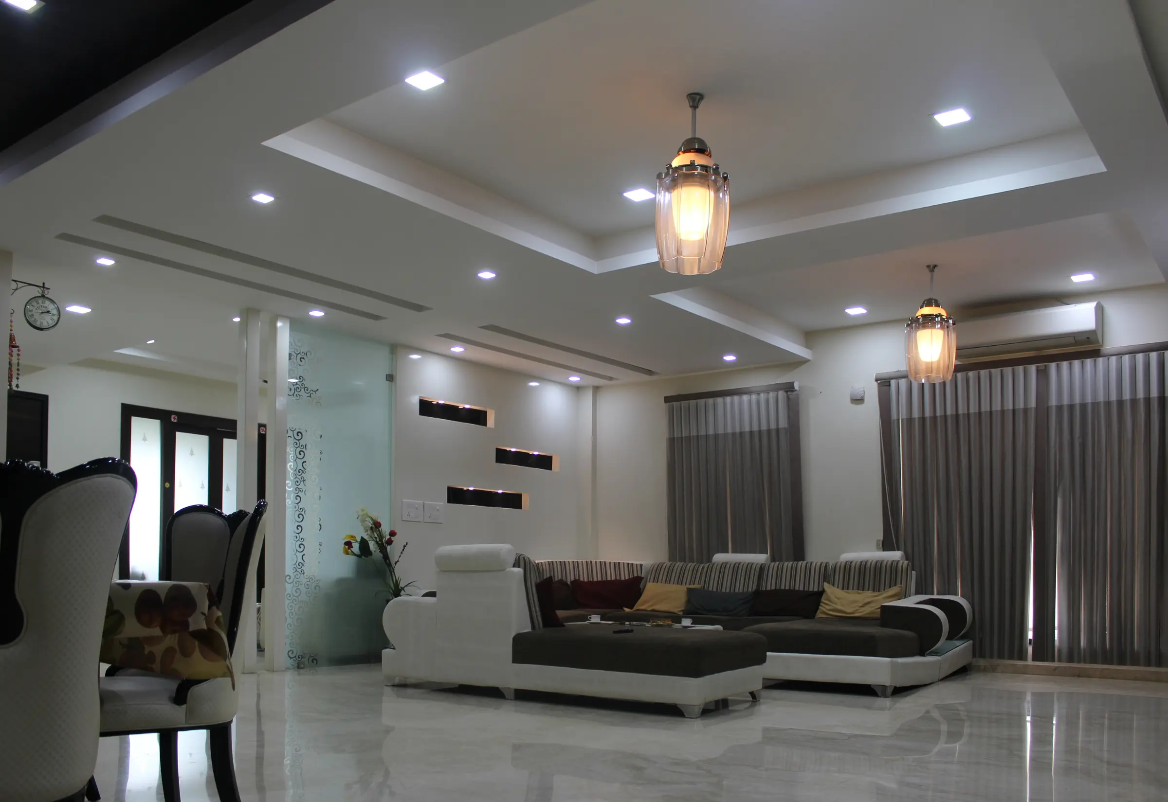 Living room with white sofas, a dark stone TV wall and a lowered ceiling with pendant lights