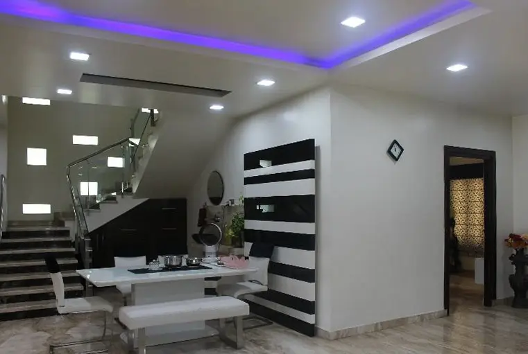 Dining area with a black-and-white striped wall, a glass-railed stair and purple cove light