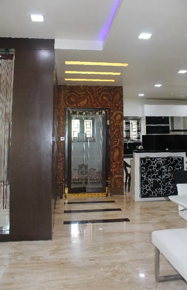 Carved timber pooja door framed by dark wood panelling and a lit ceiling slot
