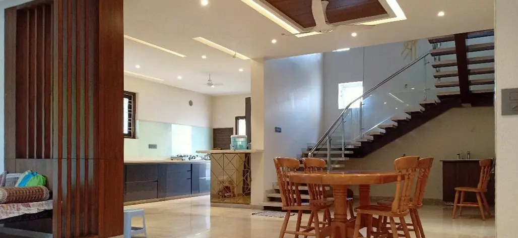 Dining area with timber chairs, a glass-railed staircase and the kitchen beyond