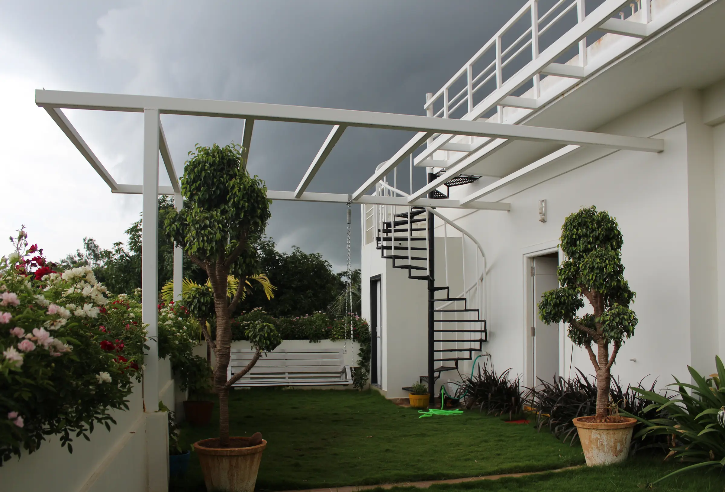 Roof terrace with a lawn, potted topiary and a white steel pergola beside a spiral stair