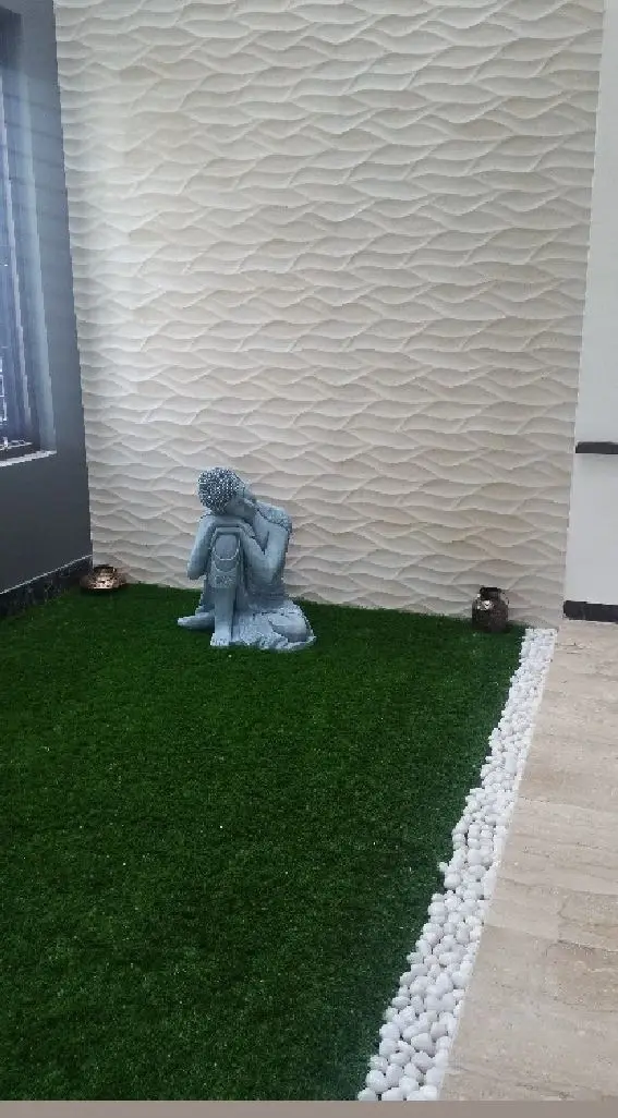 Indoor courtyard with artificial lawn, white pebbles and a Buddha statue against a textured wall