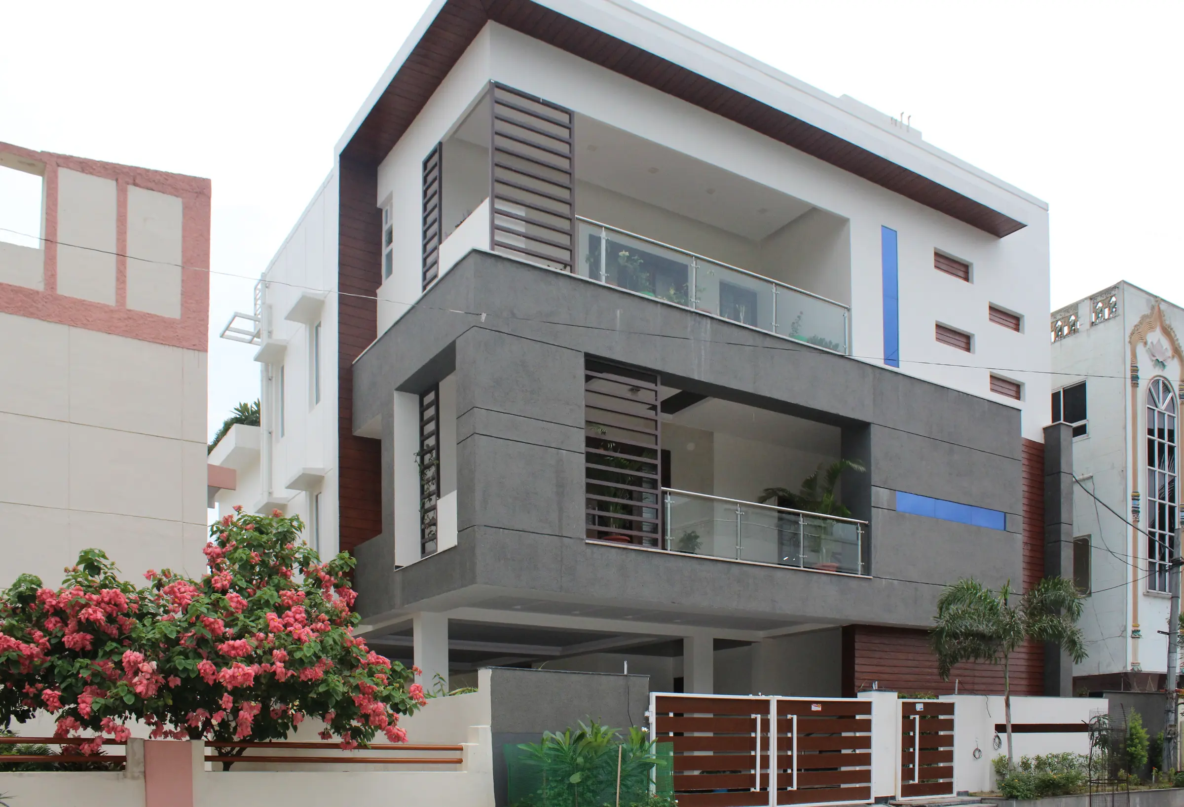 Front of the villa: a grey stone-clad upper floor with balconies above white walls, and bougainvillea at the gate