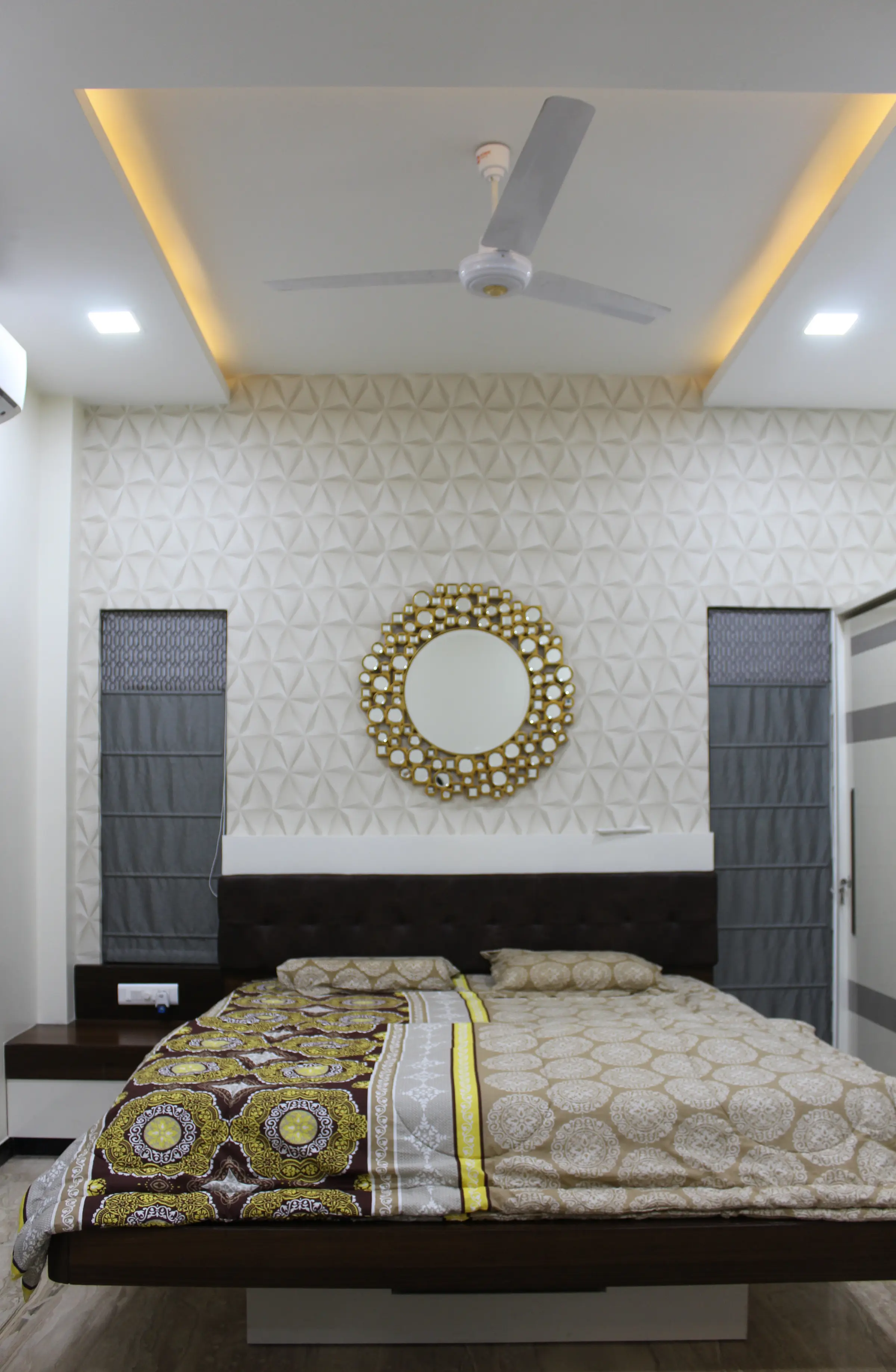 Bedroom with a patterned headboard wall and a round sunburst mirror