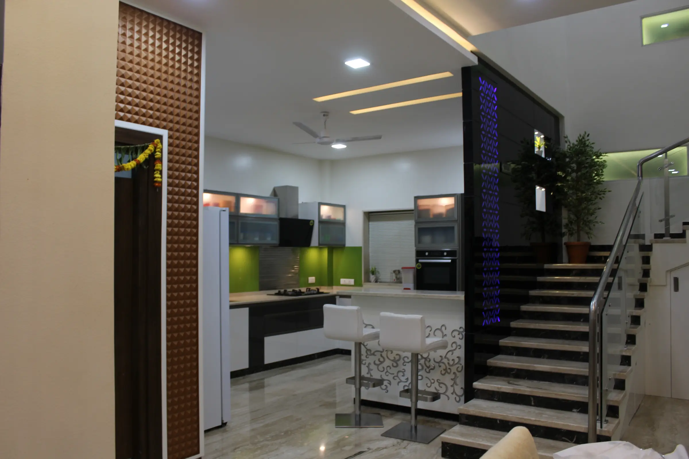 Kitchen seen past a carved timber screen and the glass-railed staircase