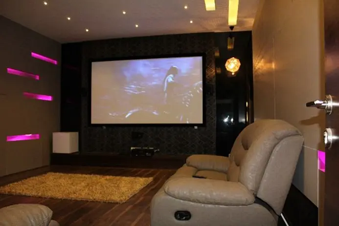 Home theatre with a projection screen, recliner seats and pink accent lights