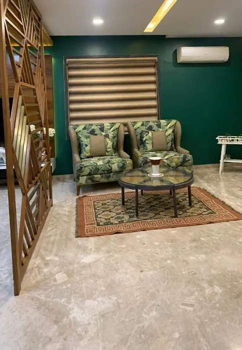 Sitting area with patterned armchairs against a deep green wall and timber blinds