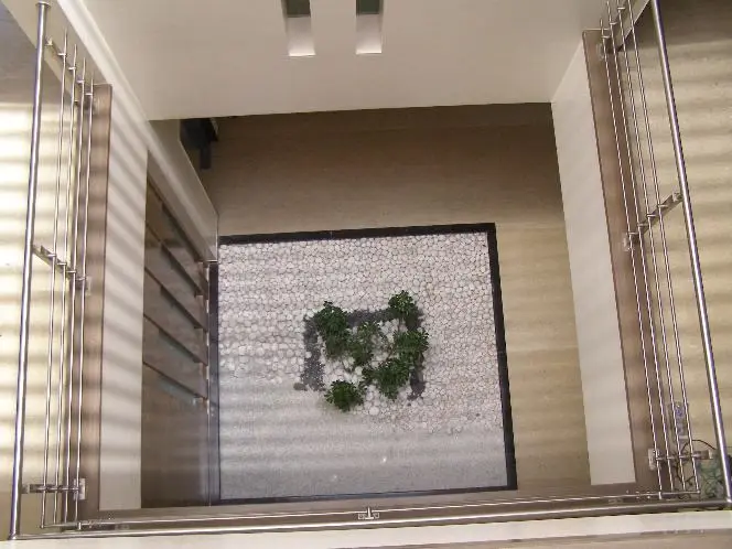 Courtyard seen from above: a white pebble bed with plants, framed by steel railings