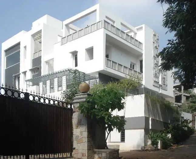 White house behind a timber-slat gate, with stone gateposts and a balcony garden